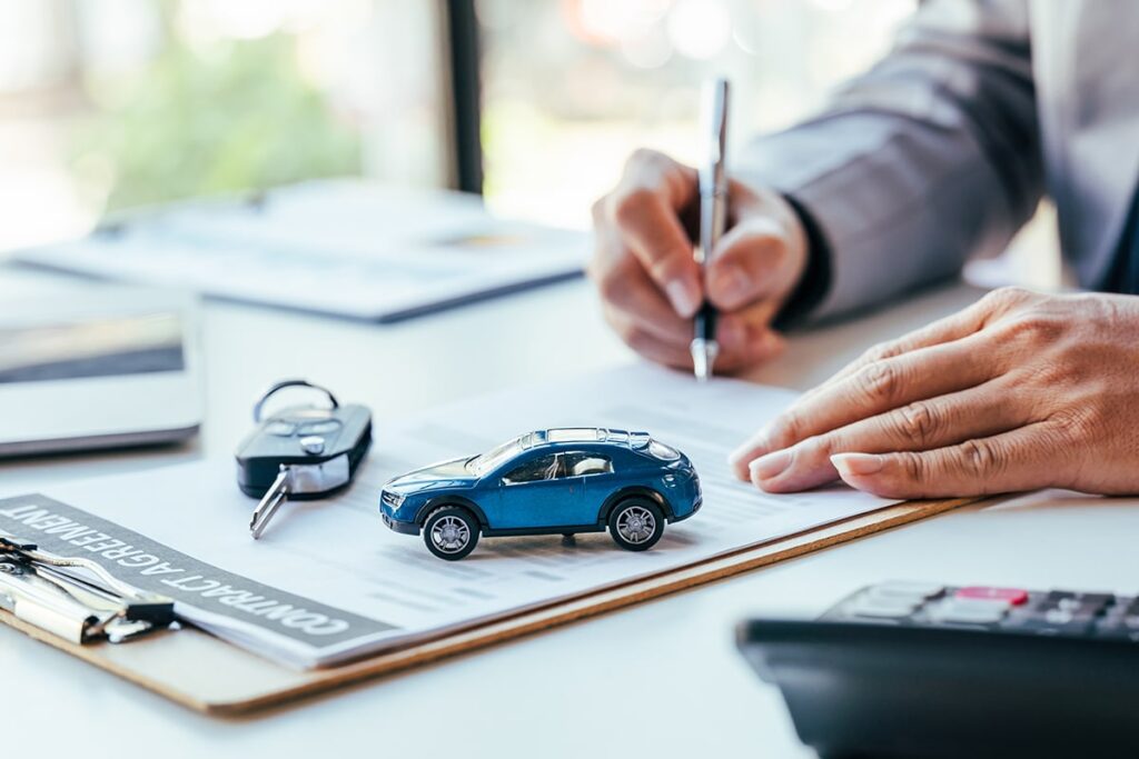 Man signing car insurance document or lease paper. Writing signature on contract or agreement. Buying or selling new or used vehicle. Car keys on table. Warranty or guarantee. Customer or salesman.